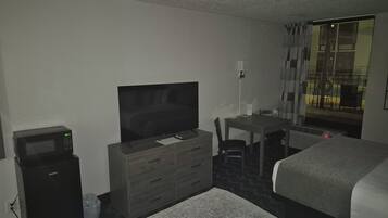 Une chambre d’hôtel équipée d’un lit, d’un bureau, d’une télévision, d’un four à micro-ondes et d’une fenêtre avec des rideaux.