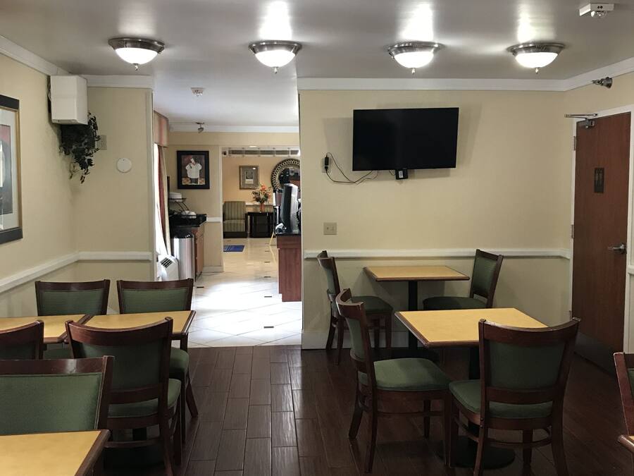 A restaurant with wooden tables and chairs, a flat-screen TV on the wall, and a ceiling with recessed lighting.