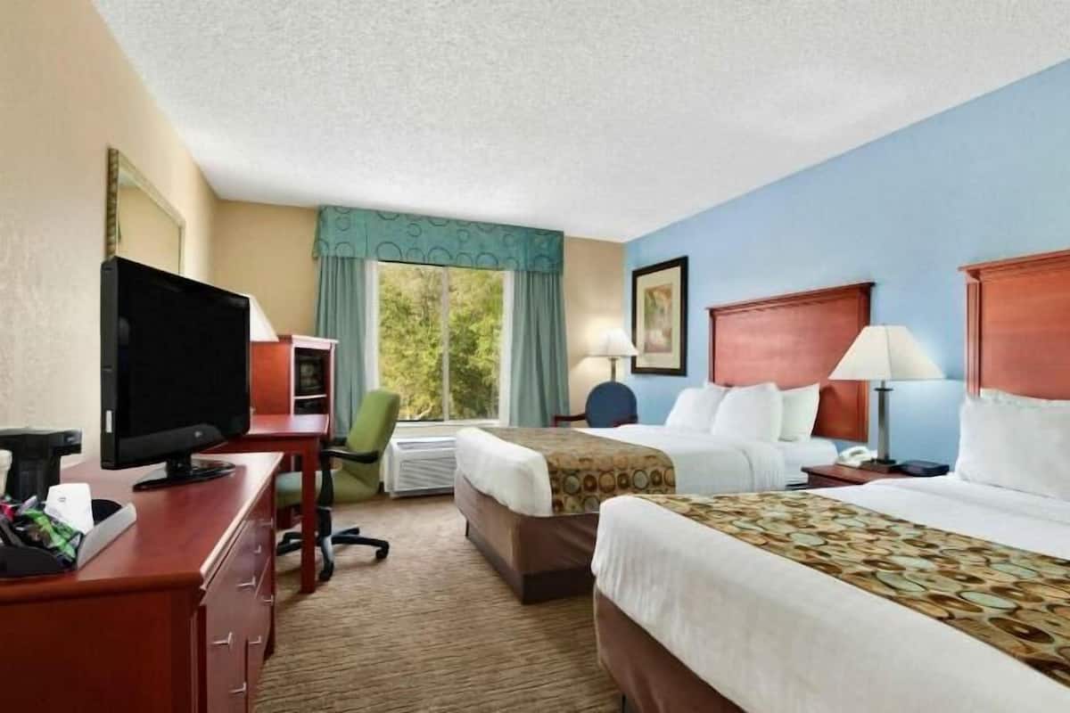 A hotel room with two beds, a desk with a computer, a TV, and a window with curtains.