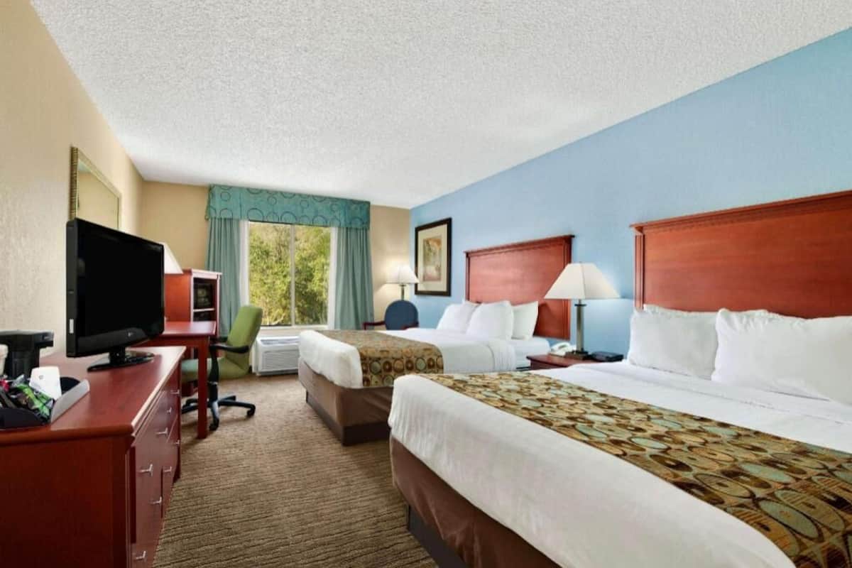 A hotel room with two beds, a desk with a TV, a chair, and a window with curtains.