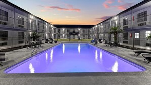 Ein modernes Hotel mit einem zentral gelegenen Schwimmbad, Sitzgelegenheiten im Freien und einem überdachten Bereich.
