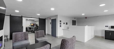 A modern hotel lobby with seating areas, a reception desk, and a kitchen area.