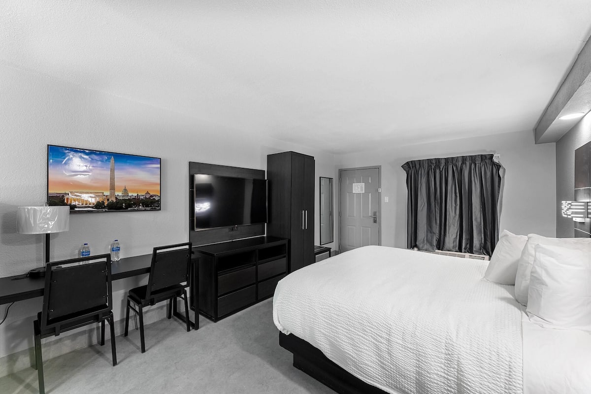 Una habitación de hotel con una cama, un escritorio con una silla, un televisor y un cuadro en la pared.