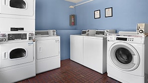 A laundry room with stacked washers and dryers, a blue wall, and a tiled floor. - Kings Inn Anaheim at the Park & Convention Center (Anaheim)