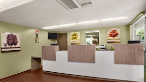 A reception area with a wooden reception desk, green walls, and artwork depicting trees. - Kings Inn Anaheim at the Park & Convention Center (Anaheim)