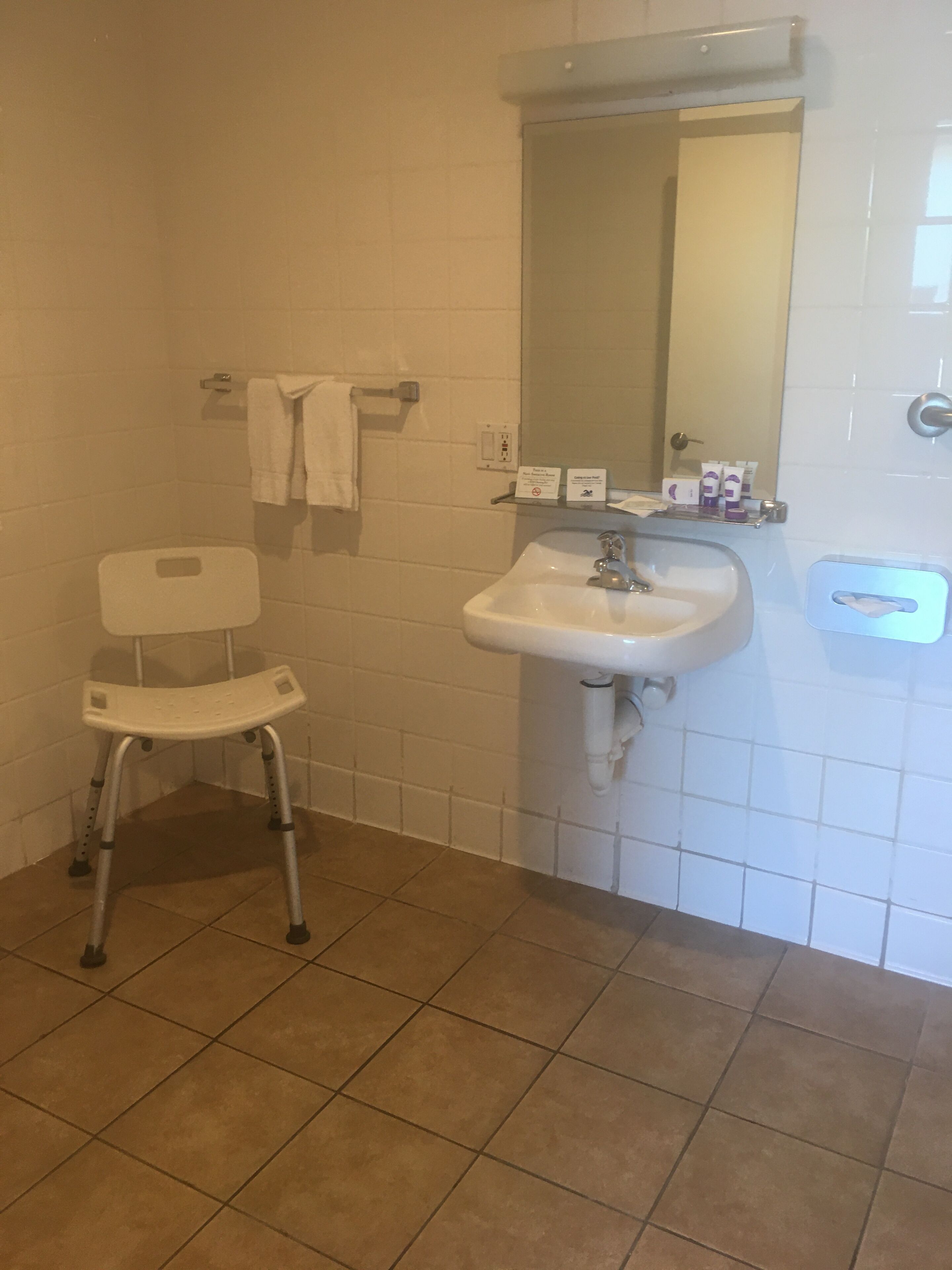 A bathroom with a white sink, a mirror, a white chair, and a towel rack.
