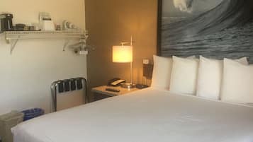 A hotel room with a large bed, a nightstand with a lamp, a phone, and a painting of a wave on the wall.