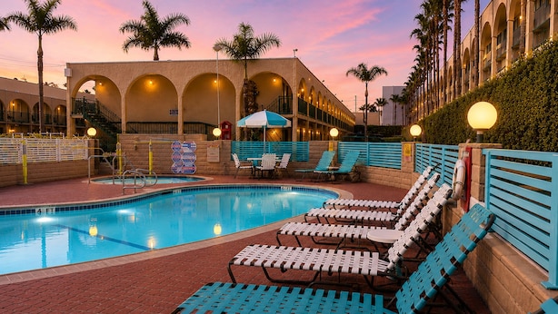 A swimming pool with lounge chairs and umbrellas, a brick pathway, and a building with arches and balconies. - Kings Inn Anaheim at the Park & Convention Center (Anaheim)