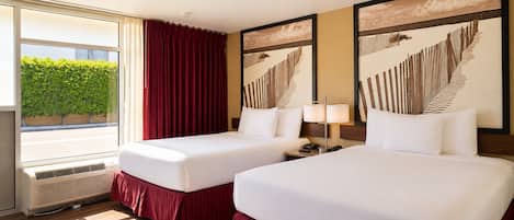 Habitación de hotel con dos camas, ventana con vista a follaje y obras de arte en las paredes.