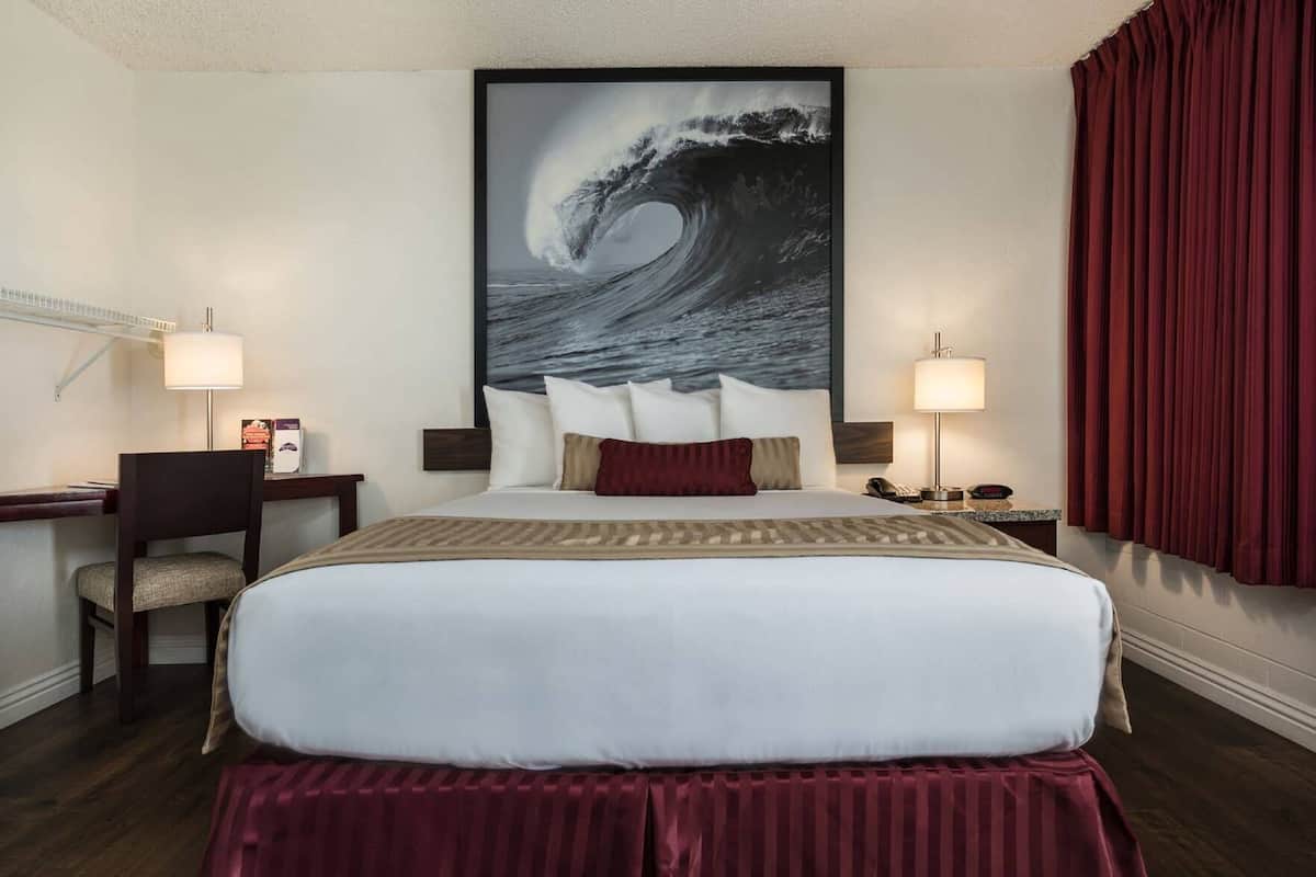 A hotel room with a large bed, a desk, a chair, two bedside lamps, and a large wave painting on the wall.