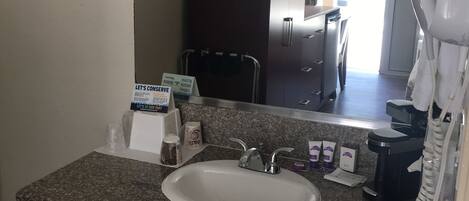 A bathroom with a granite countertop, a white sink, a large mirror, a dark wooden cabinet, and a towel rack.