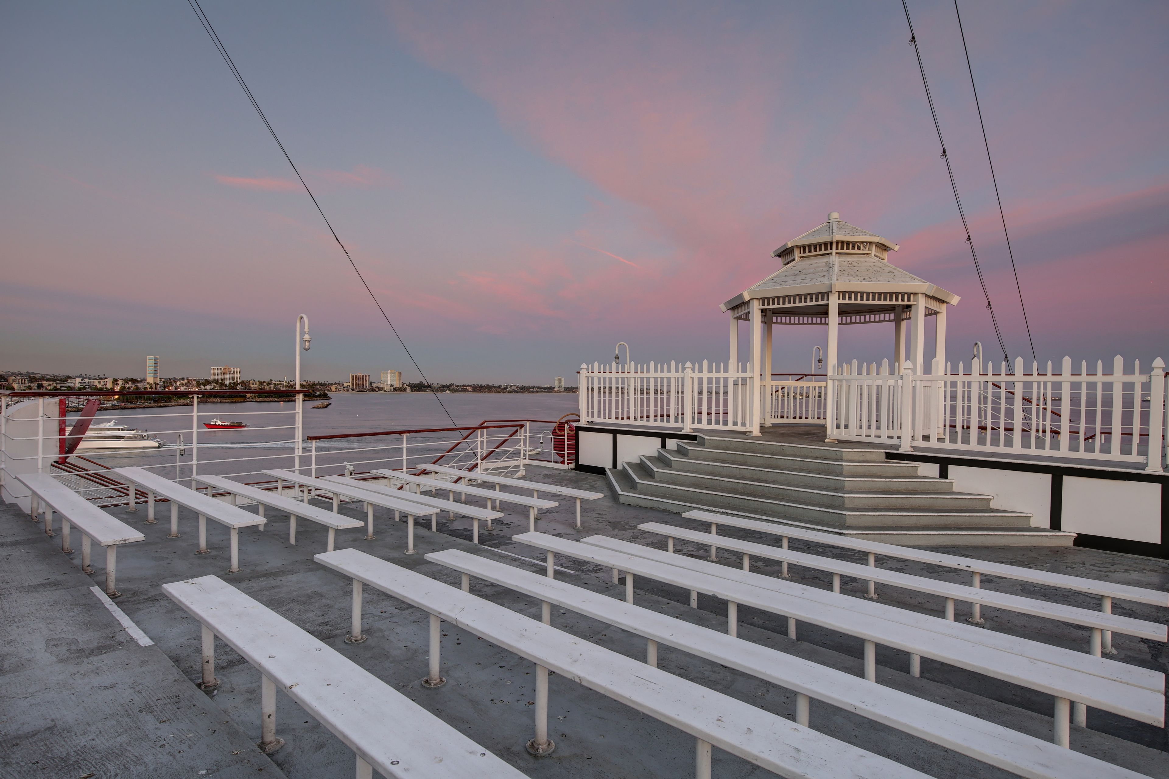 A gazebo with a white fence, white benches, and a view of the water.