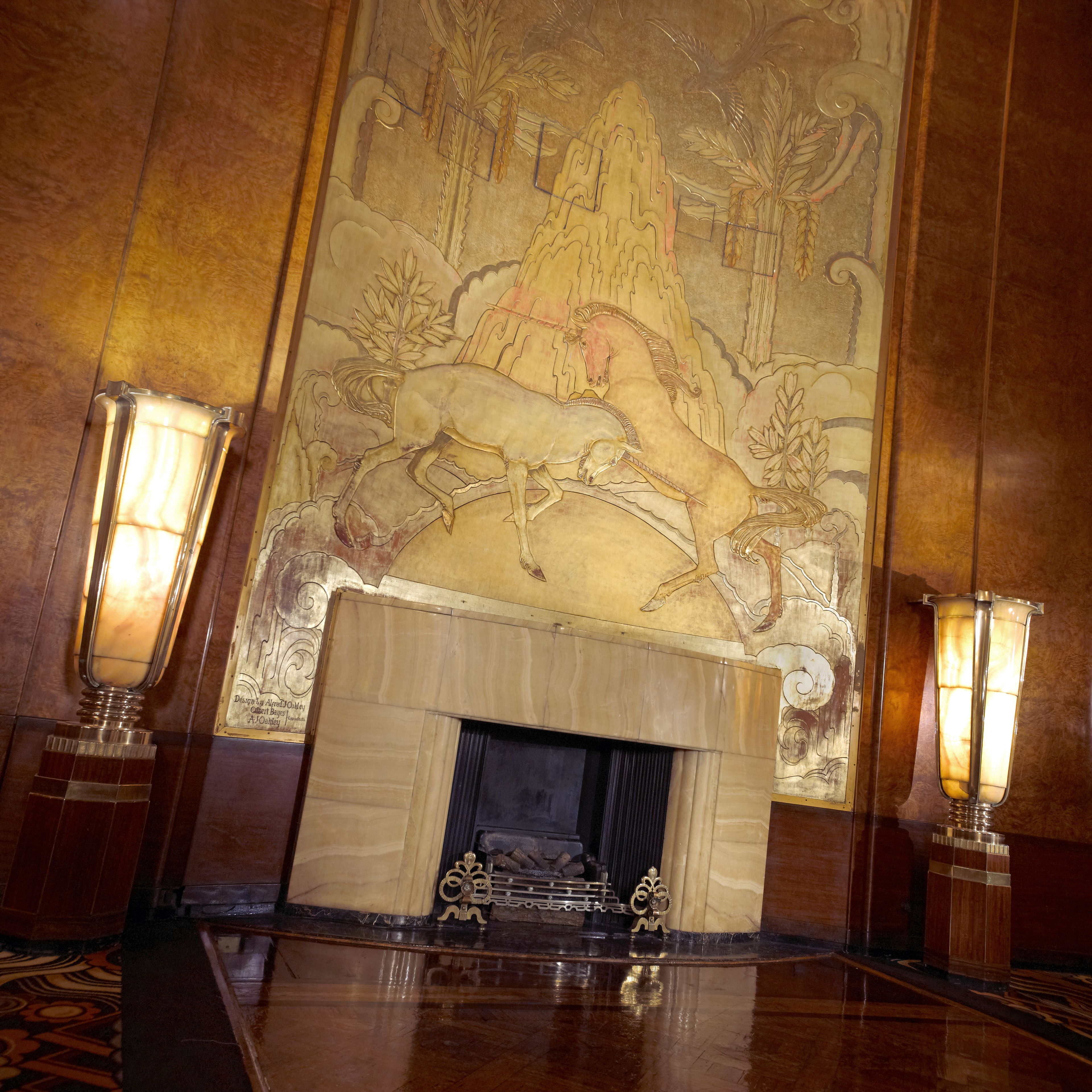 A grand hall with a large mural, a fireplace, and two ornate lamps.