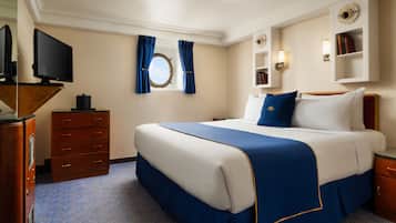 Una habitación de hotel con una cama grande, un aparador, un televisor, una ventana con cortinas y una estantería.