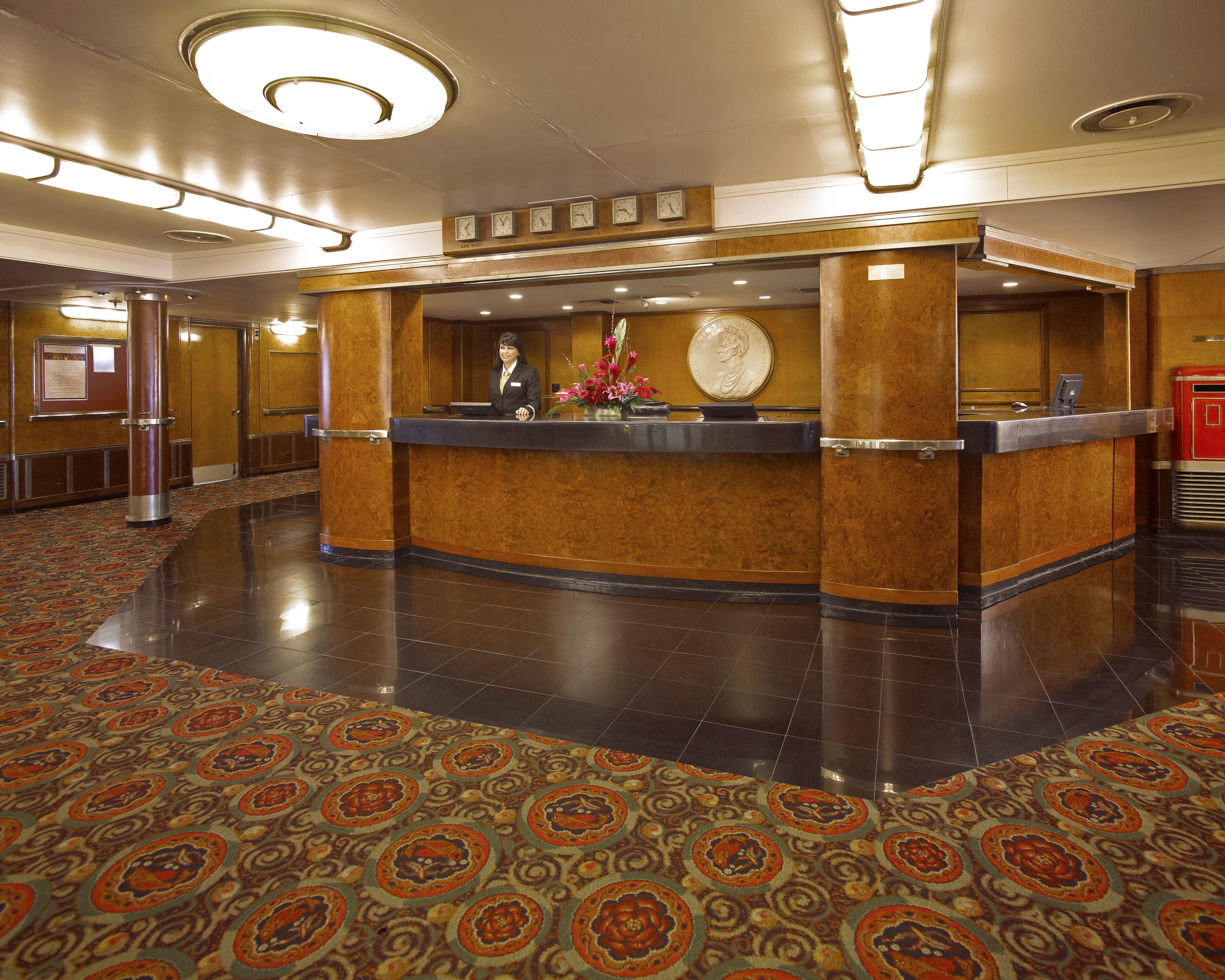A hotel reception area with a marble counter, a receptionist, and a clock on the wall.
