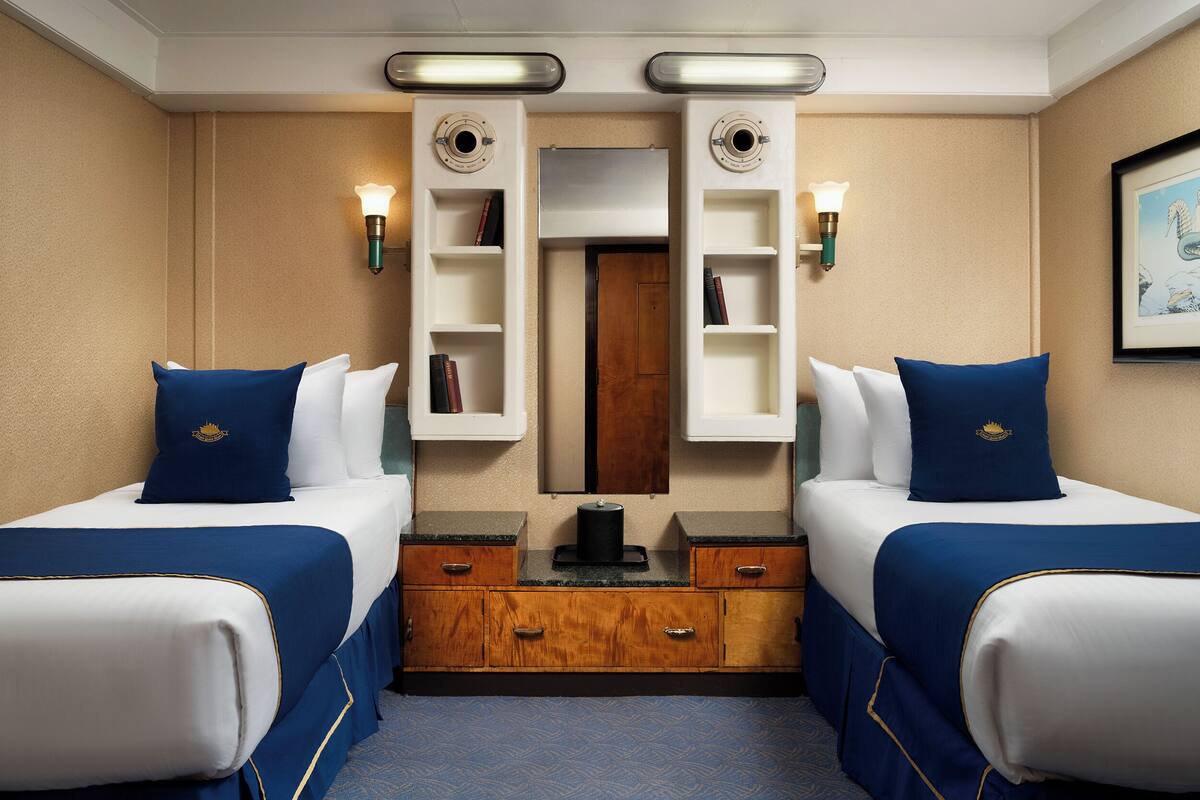 Habitación de hotel con dos camas, un aparador de madera, un espejo y estantes en la pared.
