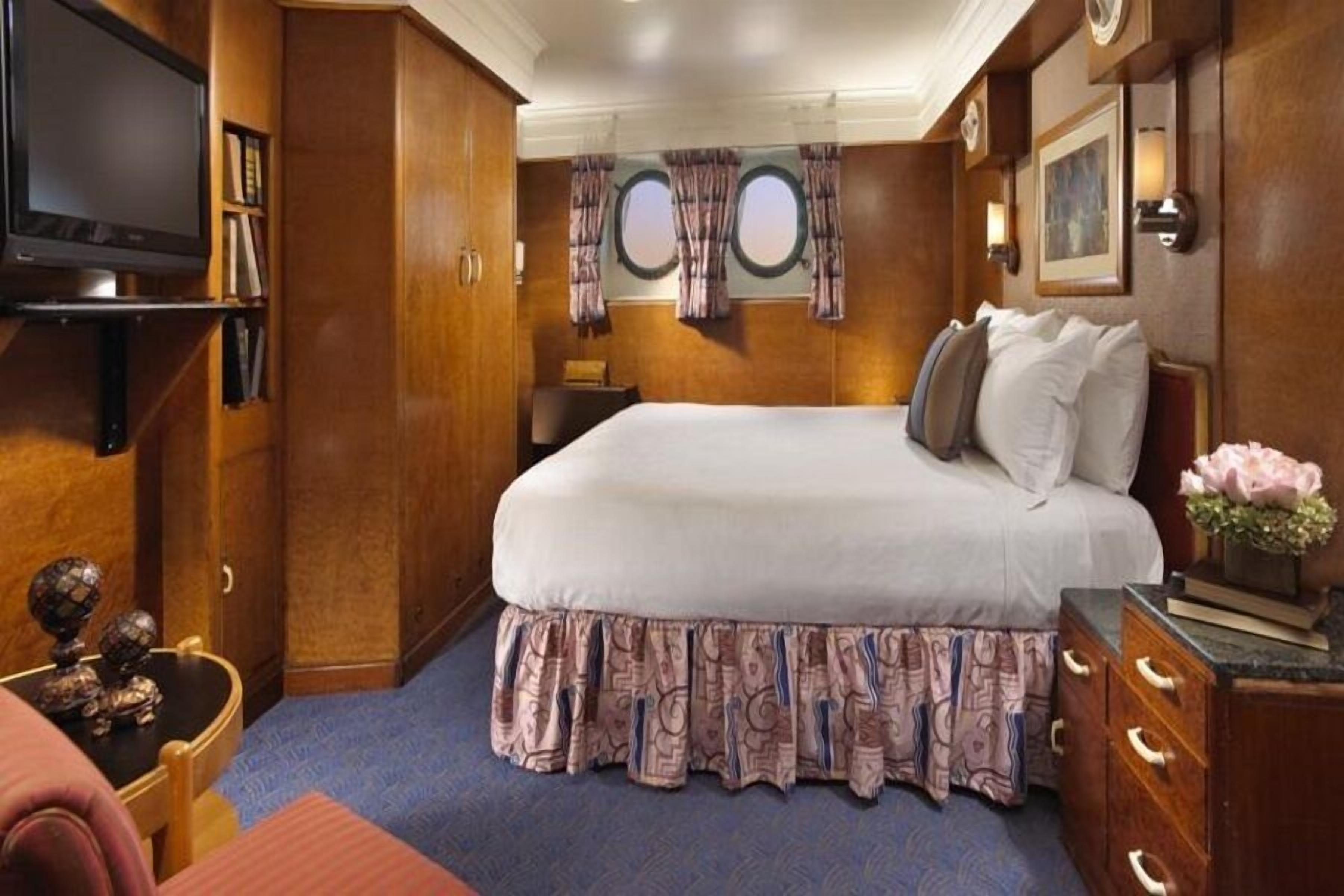A hotel room with a large bed, wooden wardrobe, a television, and a small table with decorative items.