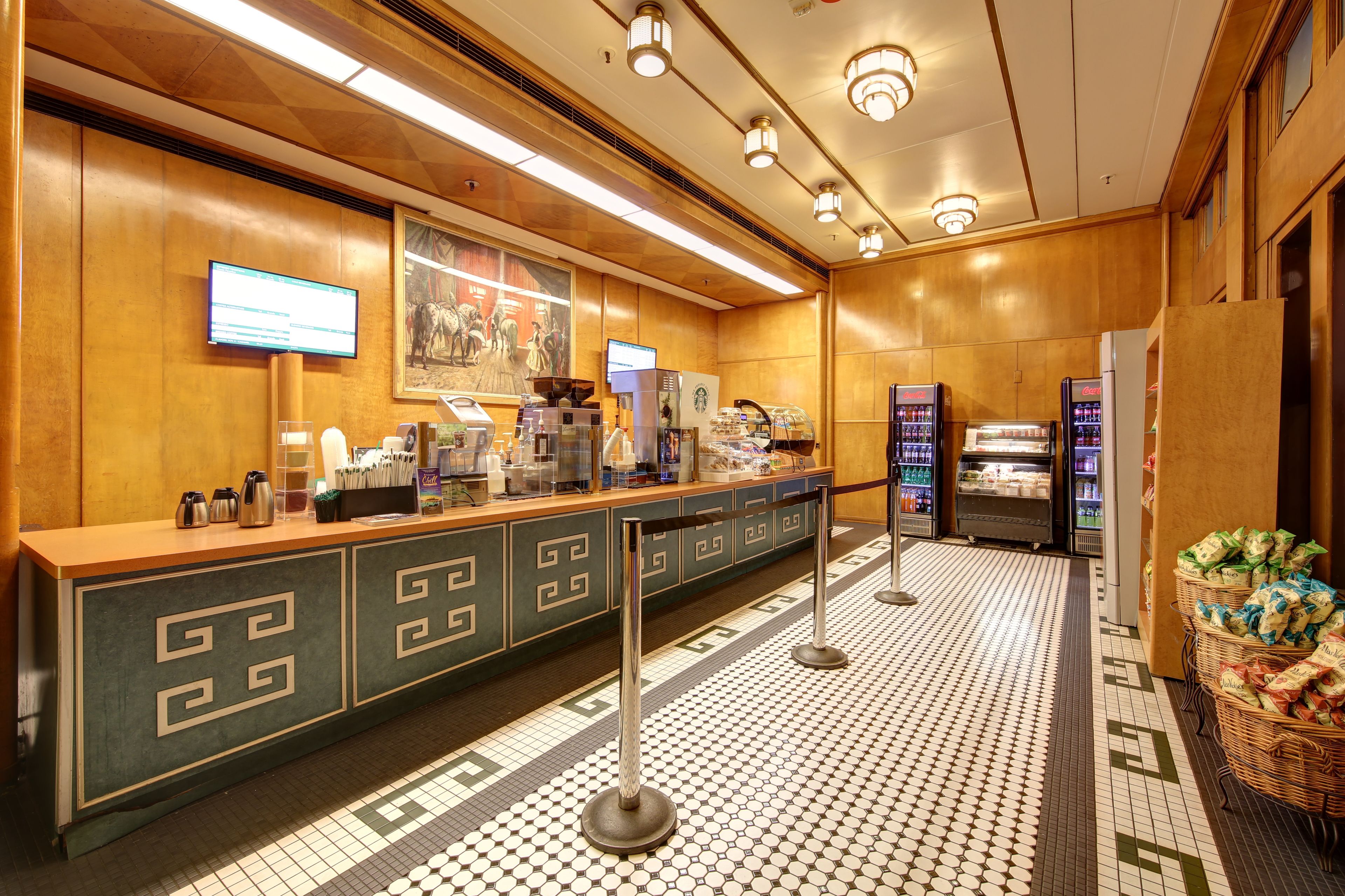 A hotel lobby with a reception desk, a coffee station, a large painting, and vending machines.