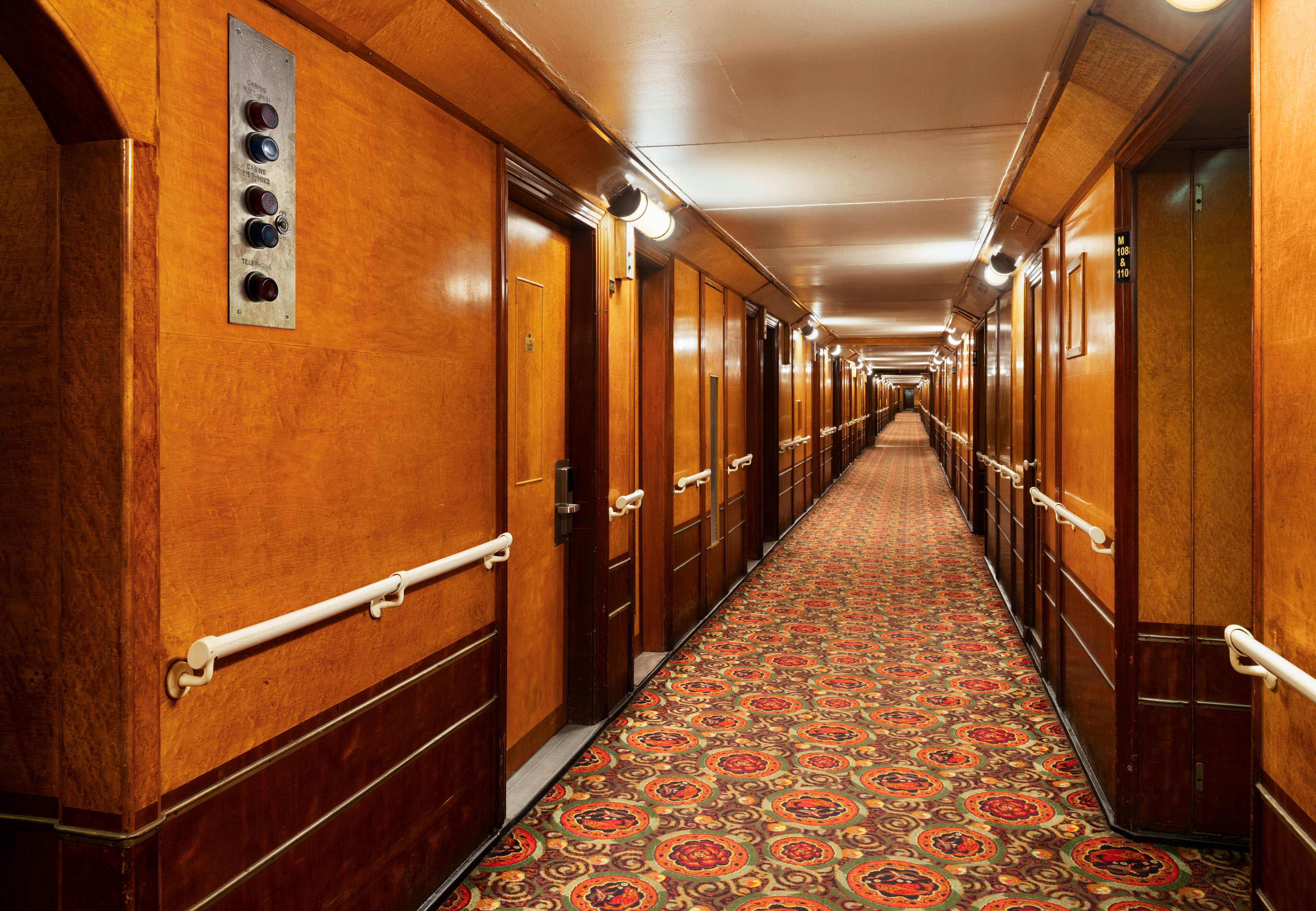 A long hallway with wooden doors and a patterned carpet.