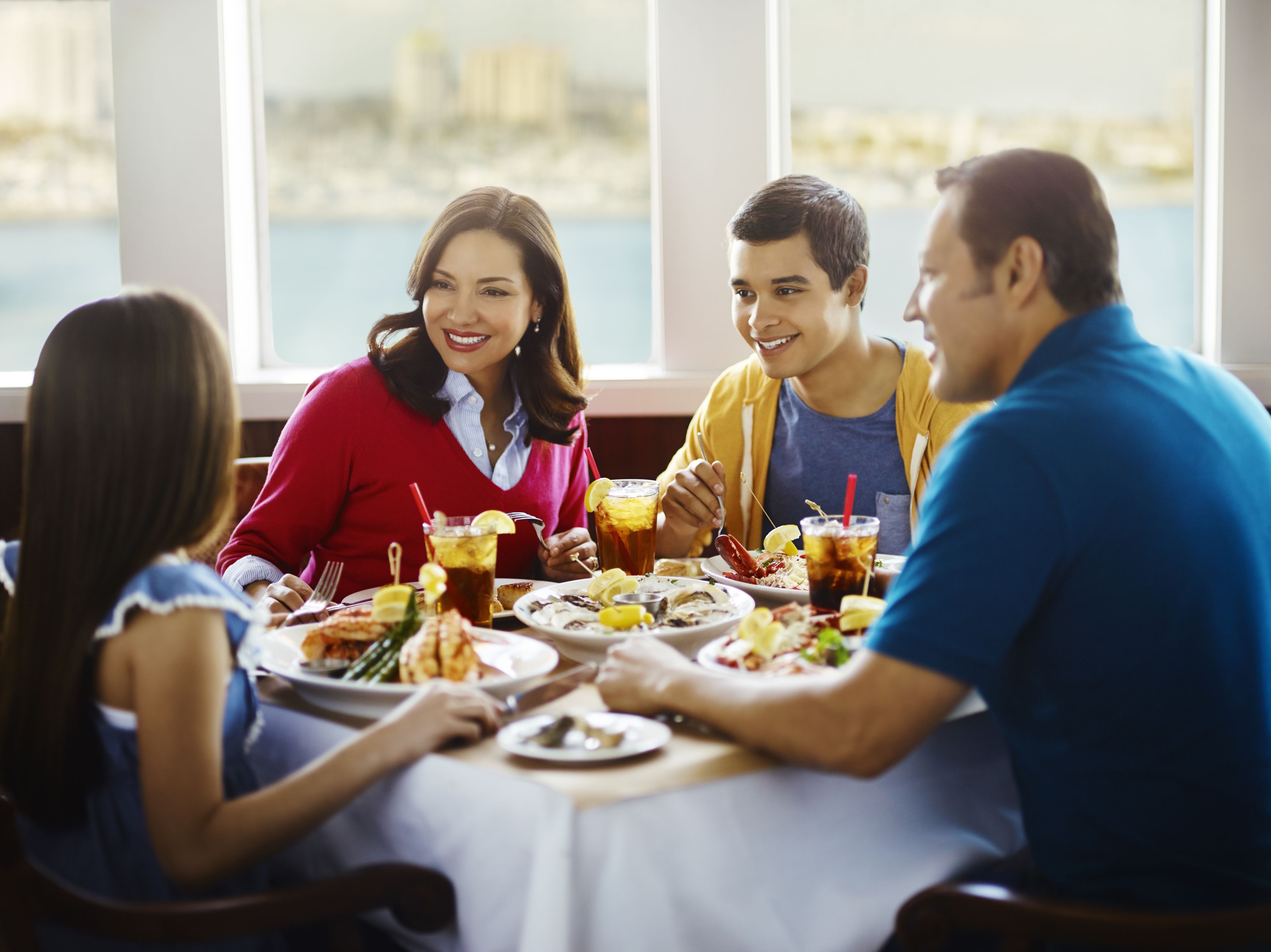A group of people dining at a table with a view of the water and buildings in the background.