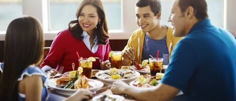 A group of people dining at a table with a view of the water and buildings in the background.