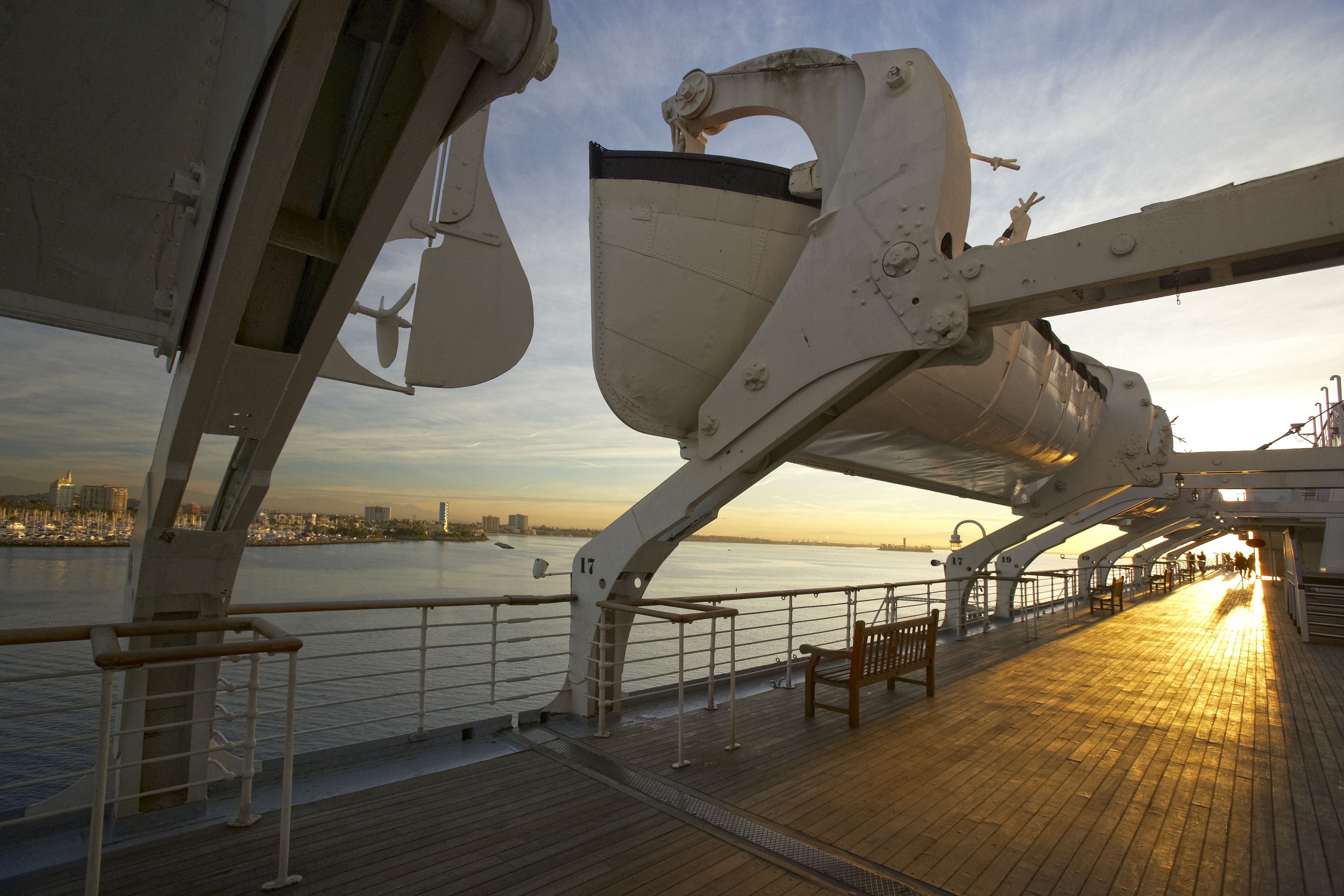 Cubierta de crucero con suelo de madera, barandillas de metal y vista del horizonte urbano al atardecer.
