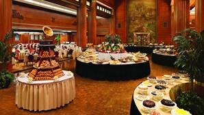Un amplio salón de banquetes con varias mesas redondas cubiertas de diversos alimentos y un bufé.