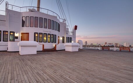 A cruise ship deck with a restaurant named "VERANDAH GRILL," wooden flooring, and a city skyline in the background.