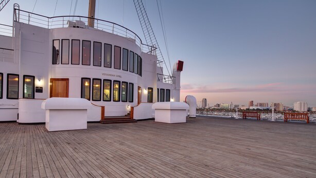 Cubierta de crucero con un restaurante llamado "VERANDAH GRILL", suelo de madera y un horizonte urbano al fondo.