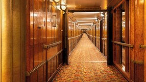 Un pasillo con puertas de madera, suelo alfombrado y un cartel que indica 'Staterooms A102-A204'.