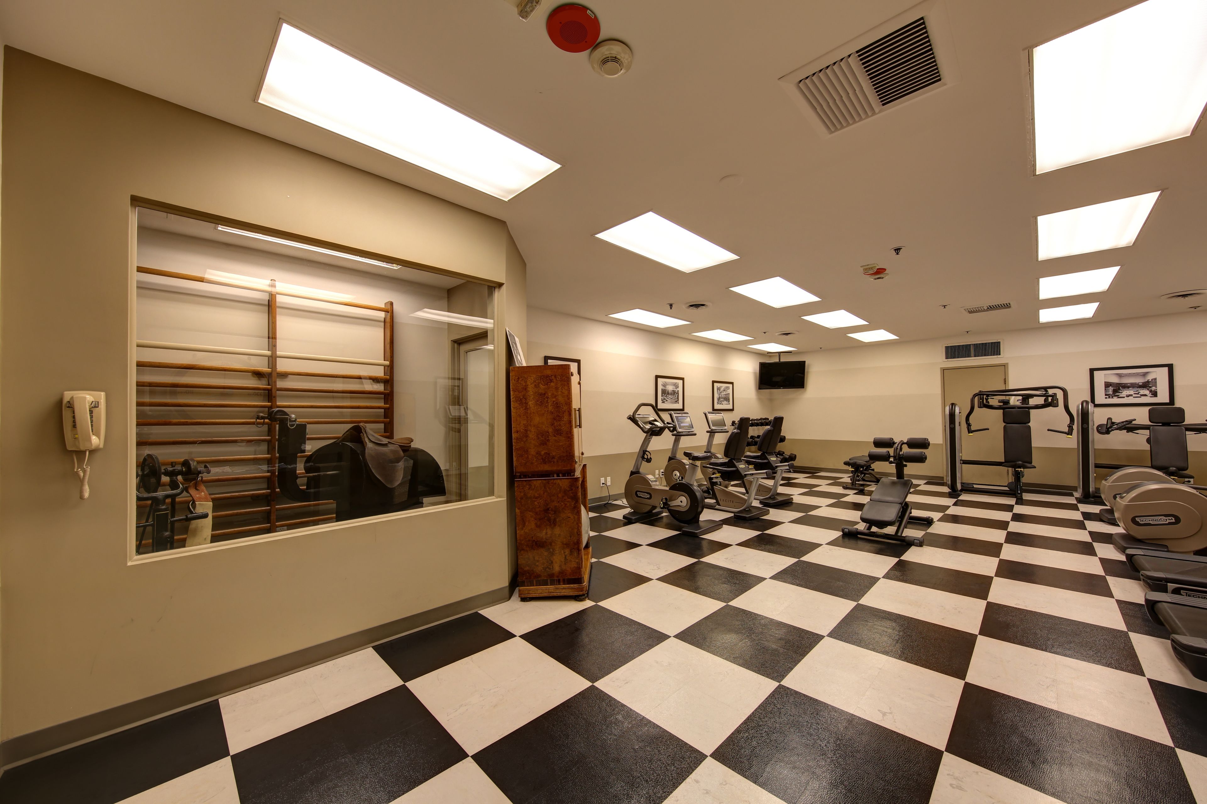Een fitnessruimte met een geruit vloertje, trainingsapparatuur en een spiegel.