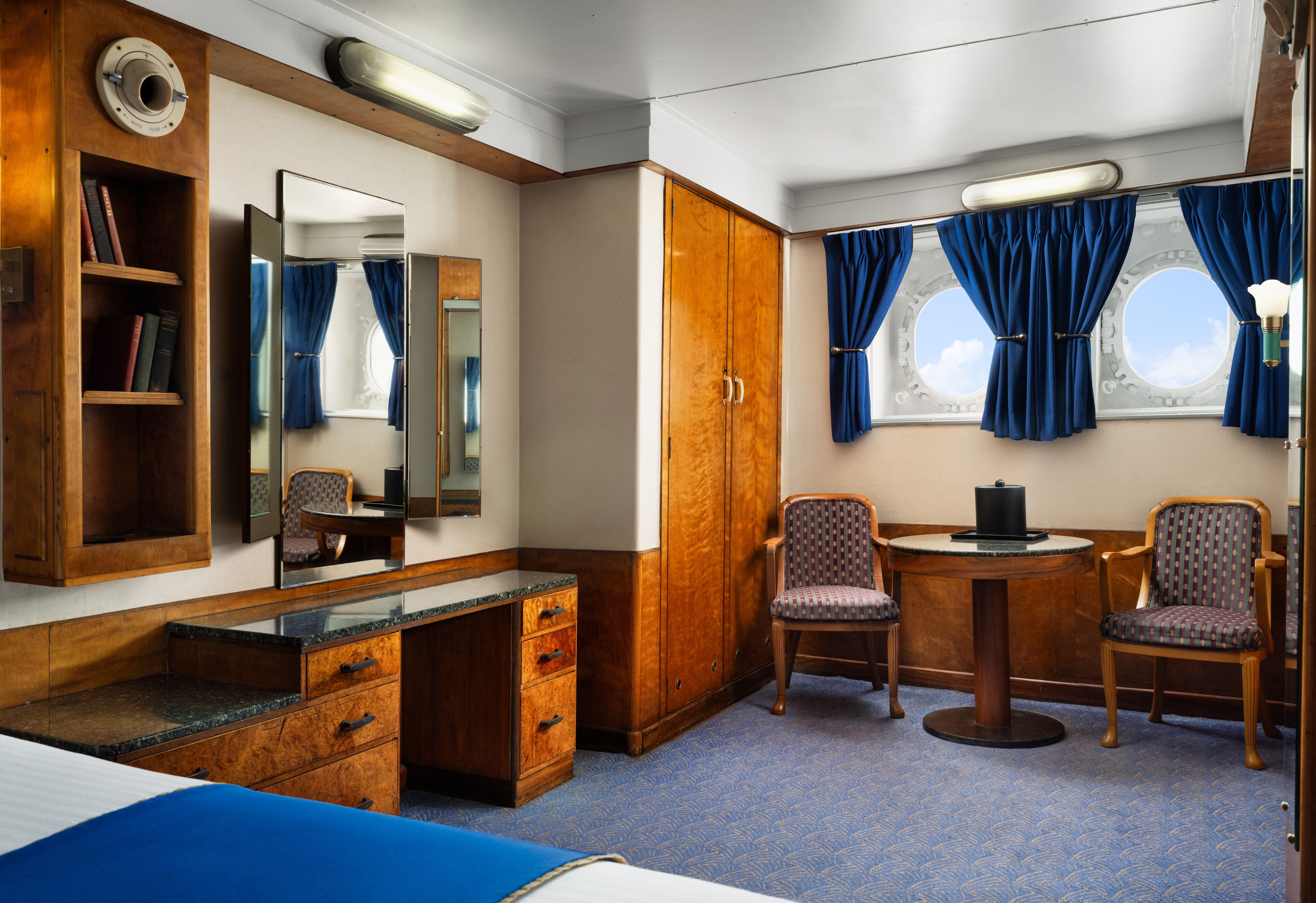 Una habitación de hotel con cama, escritorio de madera, dos sillas, espejo y armario.