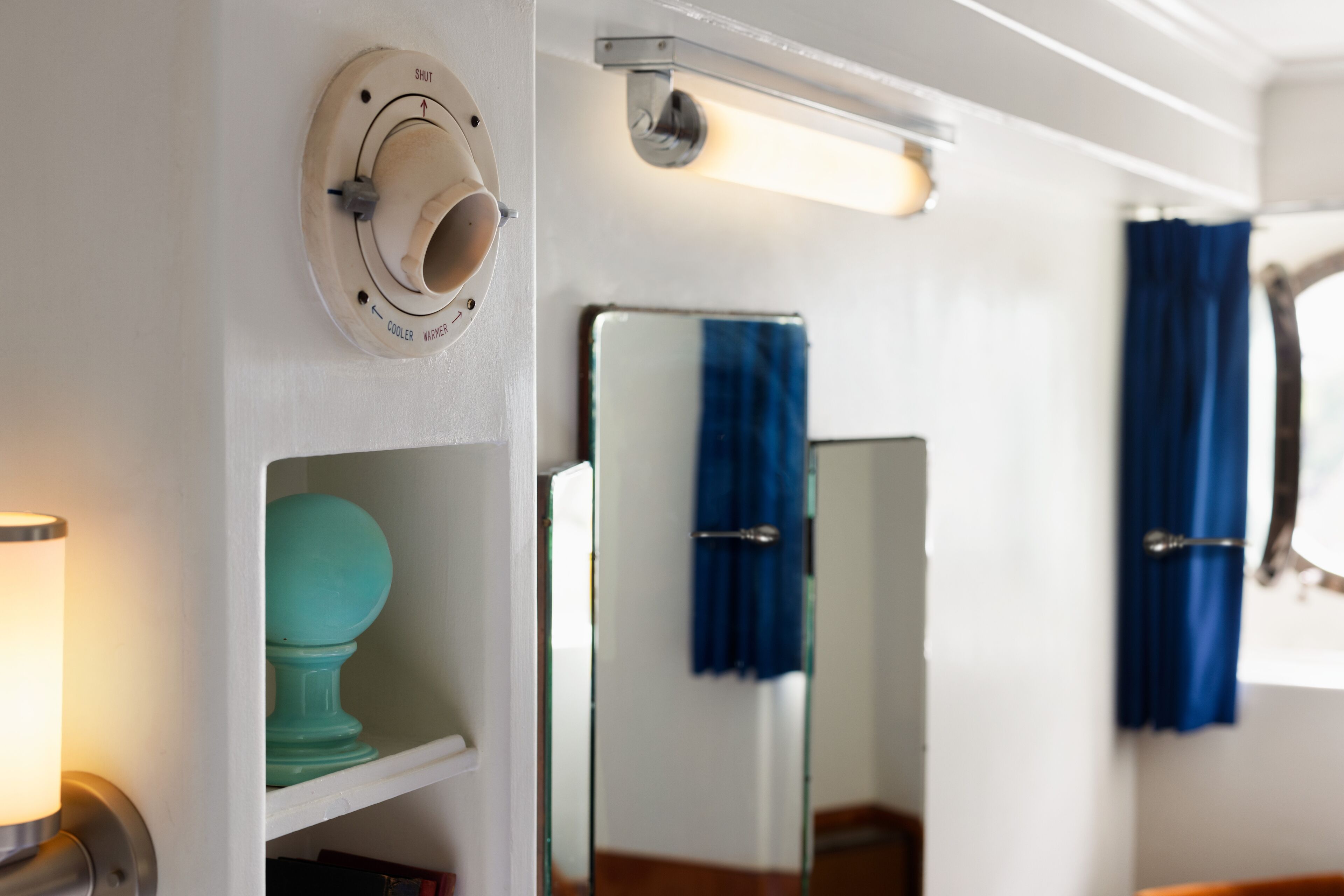 Ein Badezimmer mit weißer Wand, einem Spiegel, einem blauen Handtuch und einer Leuchte.