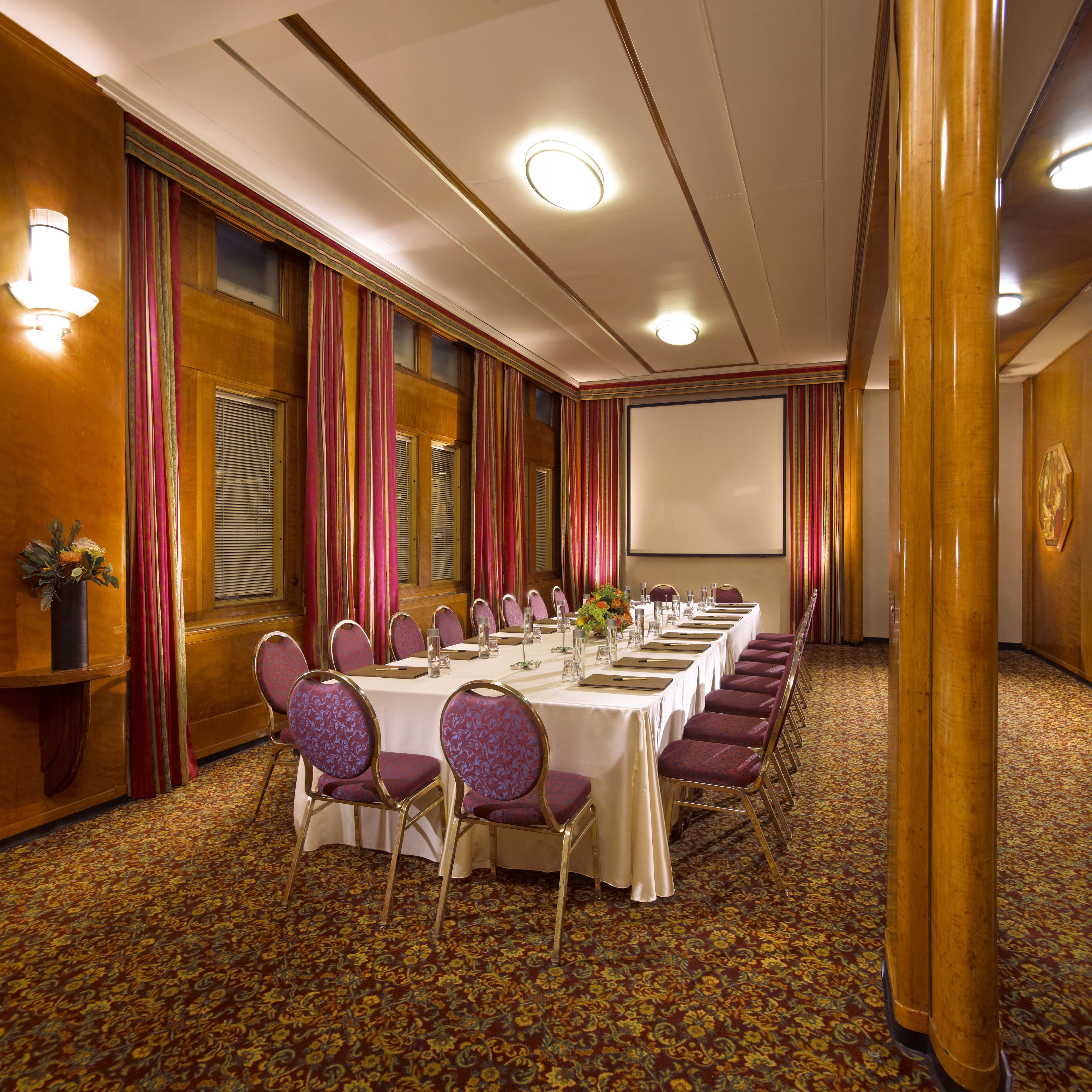 A conference room with a long table, chairs, and a projector screen.