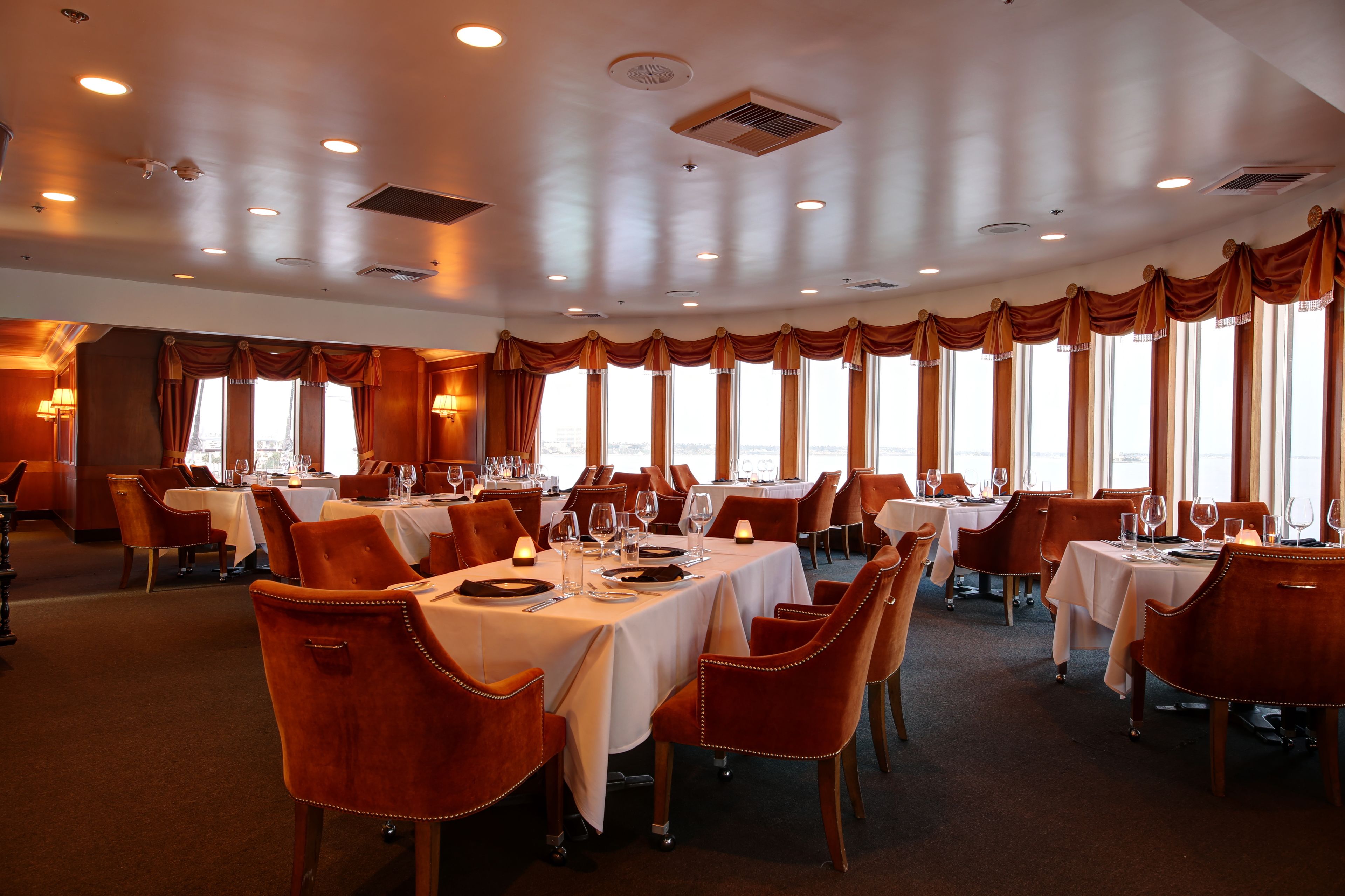 Un restaurante con varias mesas, sillas y ventanas amplias.