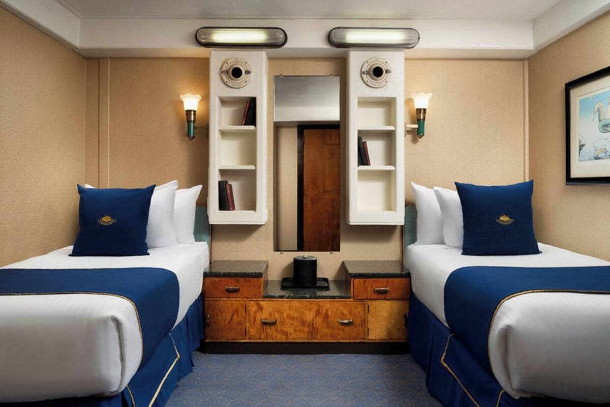 A hotel room with two beds, a wooden dresser, a mirror, and wall-mounted shelves.