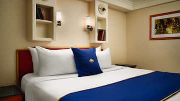 Ein Hotelzimmer mit einem großen Bett, einem Nachttisch, einem roten Sessel und Wandregalen mit Büchern und Dekoration.