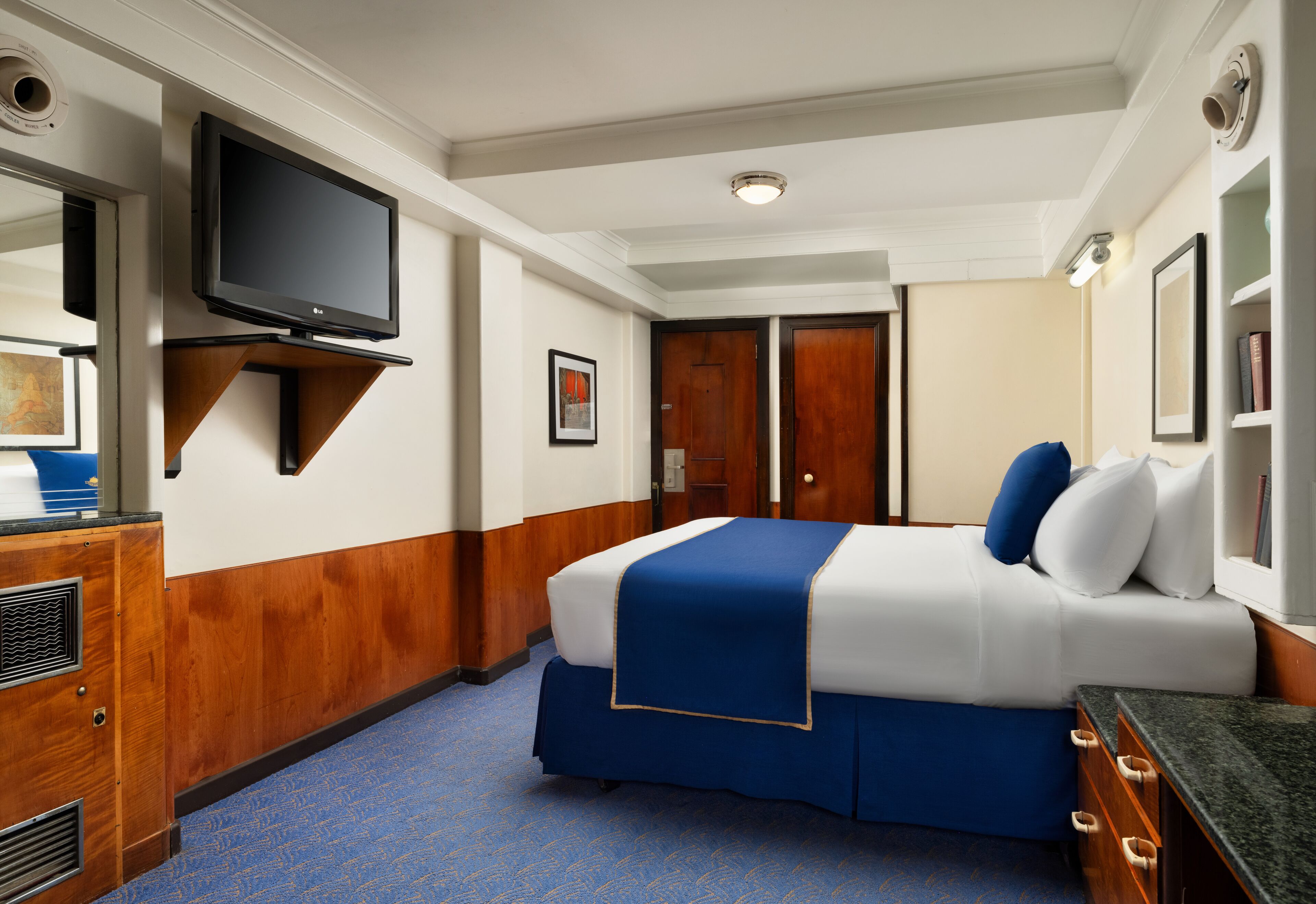Habitación de hotel con una cama, televisión montada en la pared, cómoda y una puerta.