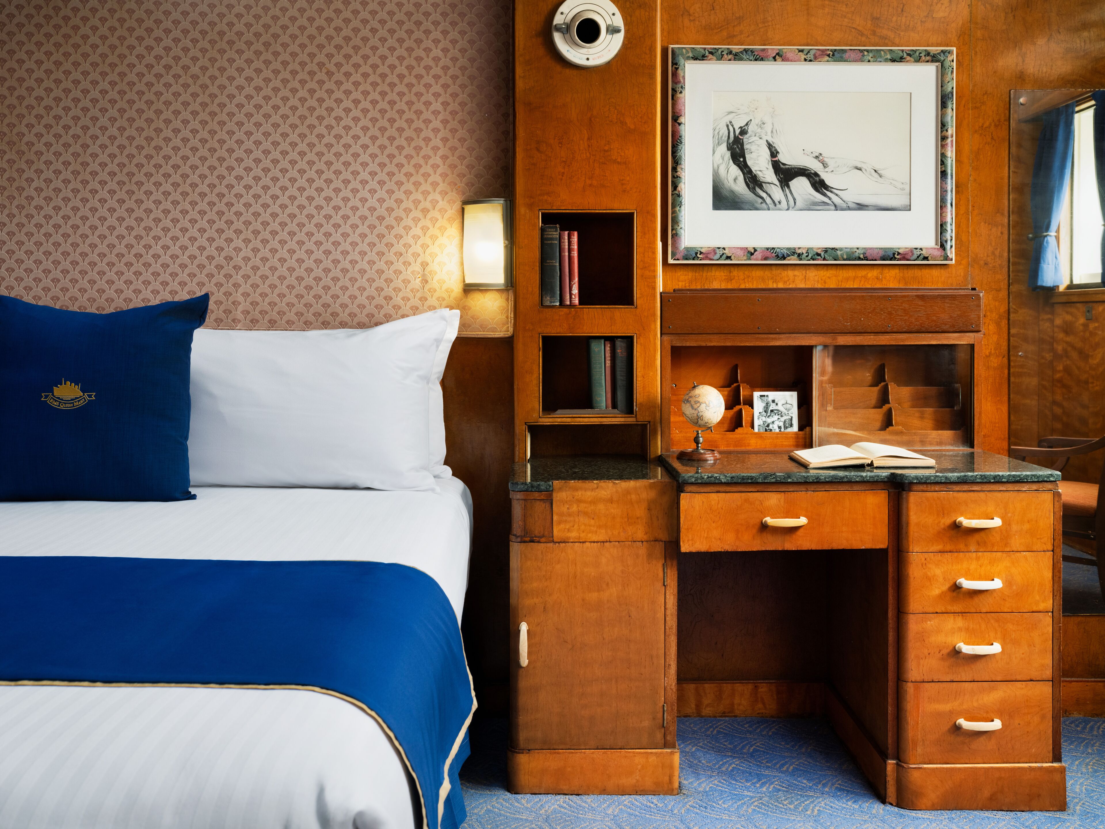 A hotel room with a bed, a wooden desk, a globe, and a framed picture on the wall.