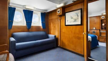 A room with a blue sofa, a wooden wardrobe, a framed picture, and a window with curtains.