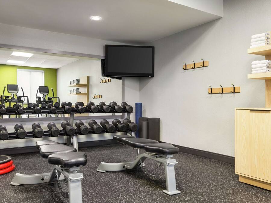 Une salle de sport équipée de bancs de musculation, d’haltères et d’un téléviseur fixé au mur.