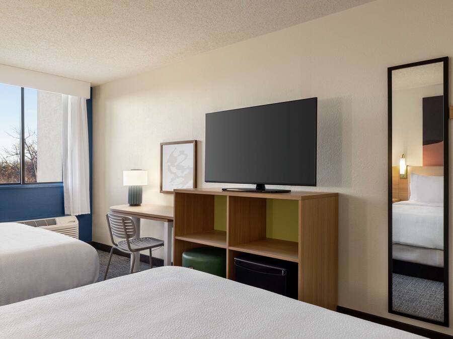 Une chambre d’hôtel avec deux lits, un bureau avec une chaise, une télévision et un grand miroir.