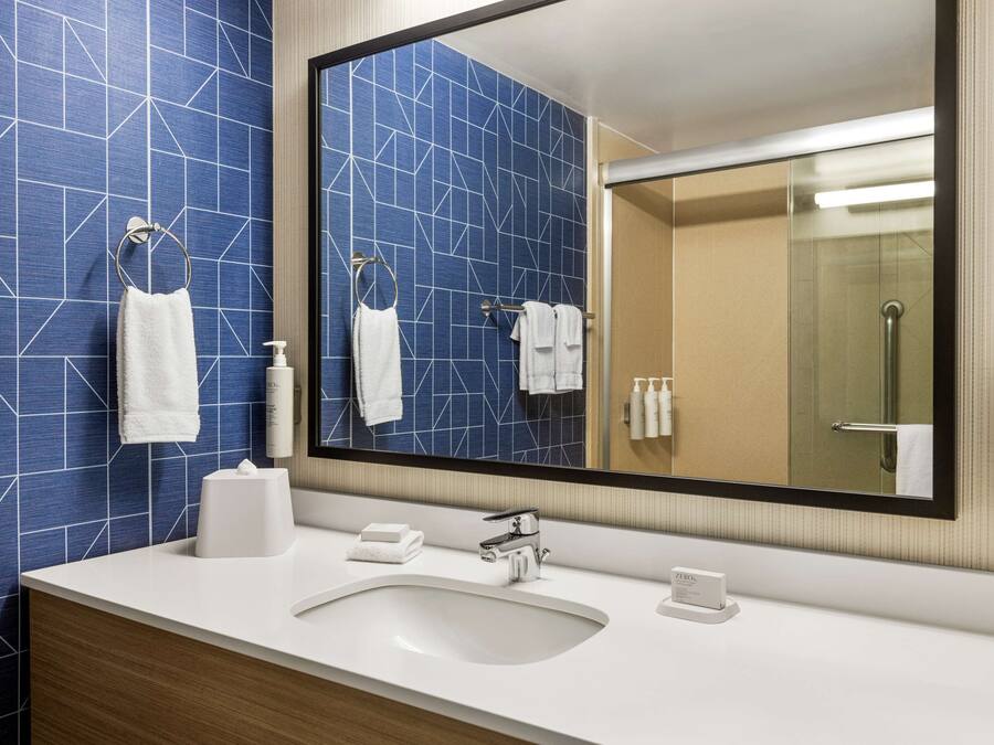 Un baño con un espejo grande, lavamanos blanco y azulejos con motivos azules.