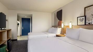 Ein Hotelzimmer mit zwei Betten, einem Fernseher, einem Schreibtisch und einer Tür zu einem Flur.