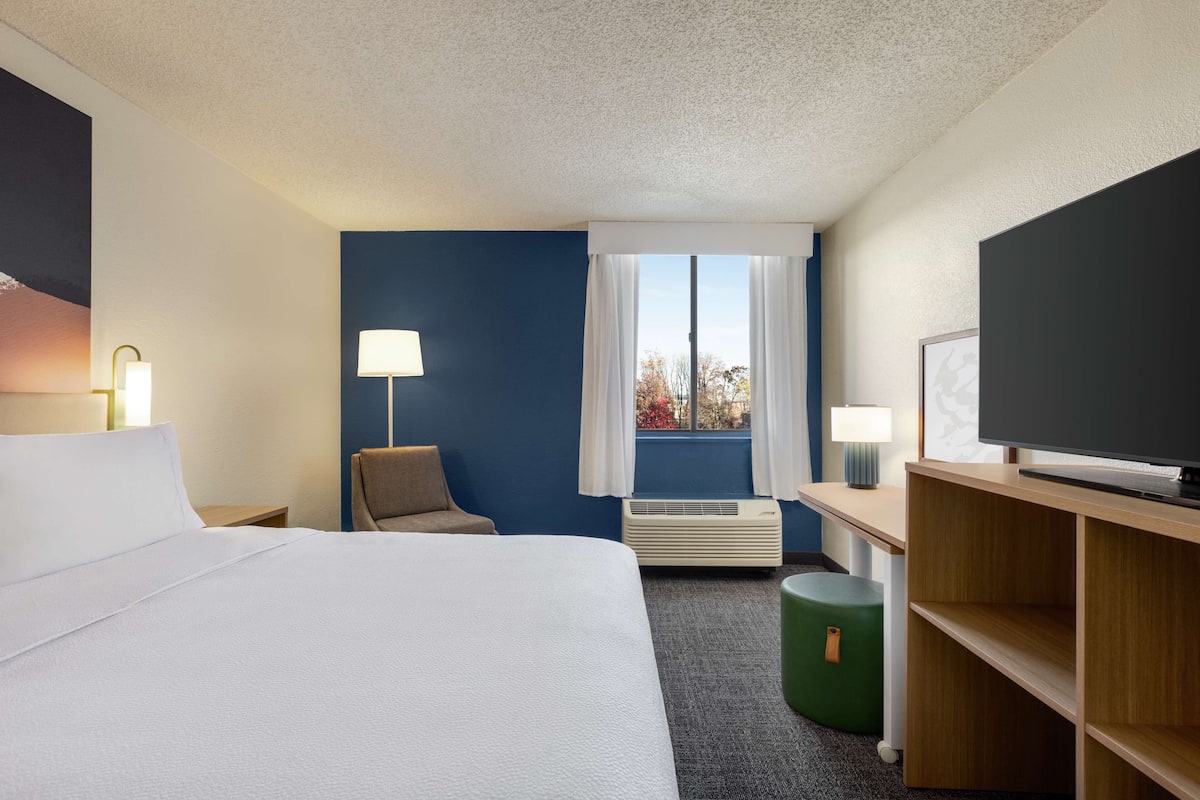 Ein Hotelzimmer mit Bett, Schreibtisch, Stuhl, Fernseher und einem Fenster mit Vorhängen.