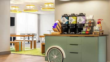 A modern kitchen area with a green cart holding coffee machines, a water dispenser, and various kitchen utensils.