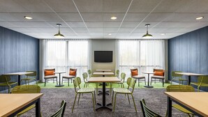 A conference room with a large table, multiple chairs, a flat-screen TV, and two windows with curtains. - Spark by Hilton Germantown Washington DC North (Germantown)