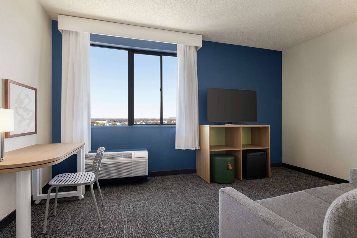 Ein Hotelzimmer mit Schreibtisch, Stuhl, Fernseher und Blick auf die Stadt.