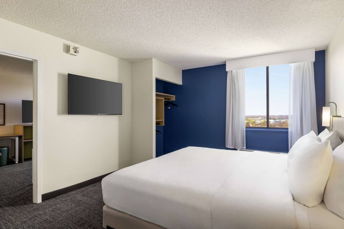 Ein Hotelzimmer mit einem großen Bett, einem Flachbildfernseher, einem Fenster mit Vorhängen und Blick auf die Stadt.