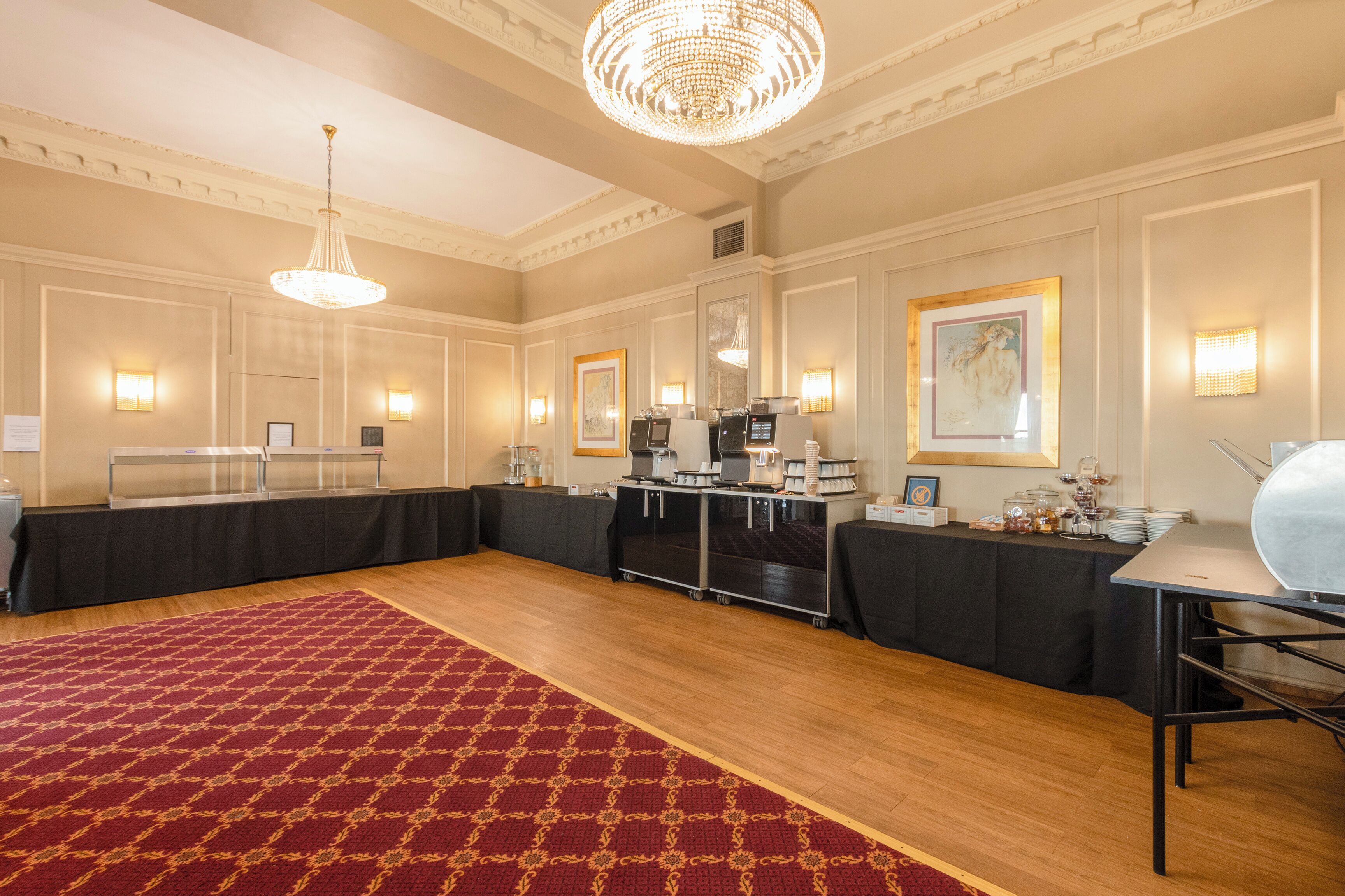 A spacious room with a red patterned carpet, a chandelier, and tables with black tablecloths.